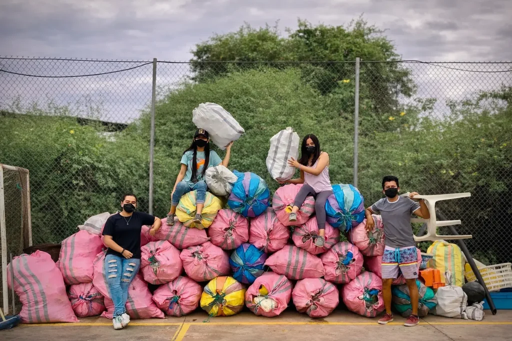Group of local volunteers collecting plastic waste in Galápagos, sitting on large bags filled with debris during a cleanup effort