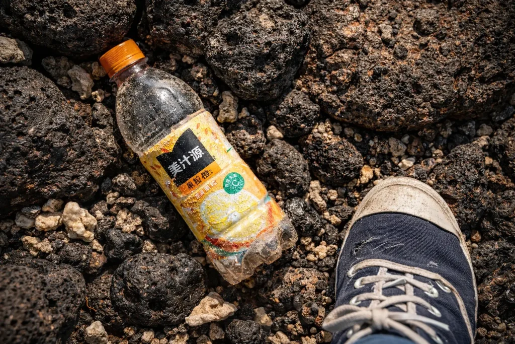 Discarded plastic bottle on volcanic rocks in Galápagos shoreline next to a person’s shoe, showing ocean-borne pollution reaching remote ecosystems