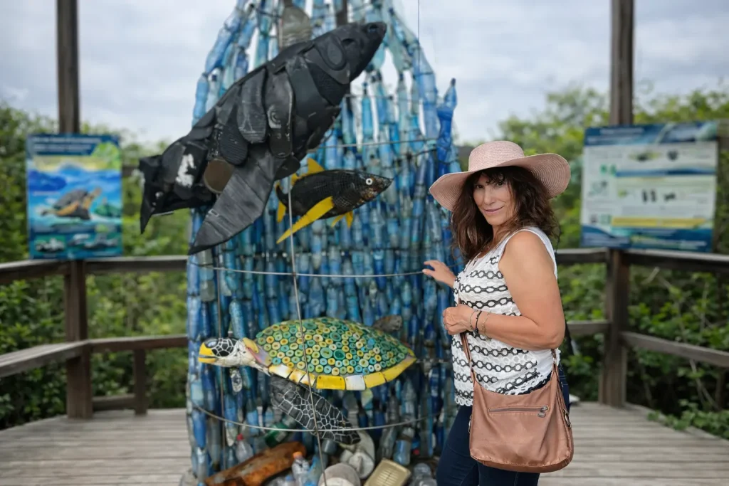 A woman stands beside an artistic installation made from collected plastic waste on Santa Cruz Island, Galápagos, featuring marine animals shaped from recycled materials.