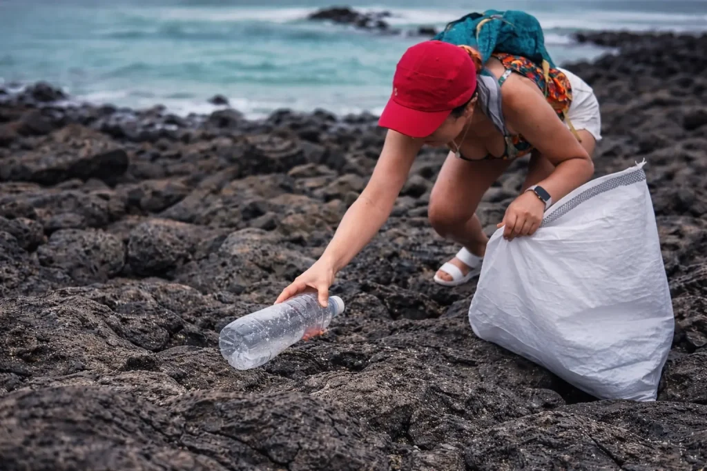 A woman picks up a plastic bottle from volcanic rocks along the Galápagos shoreline during a coastal cleanup.