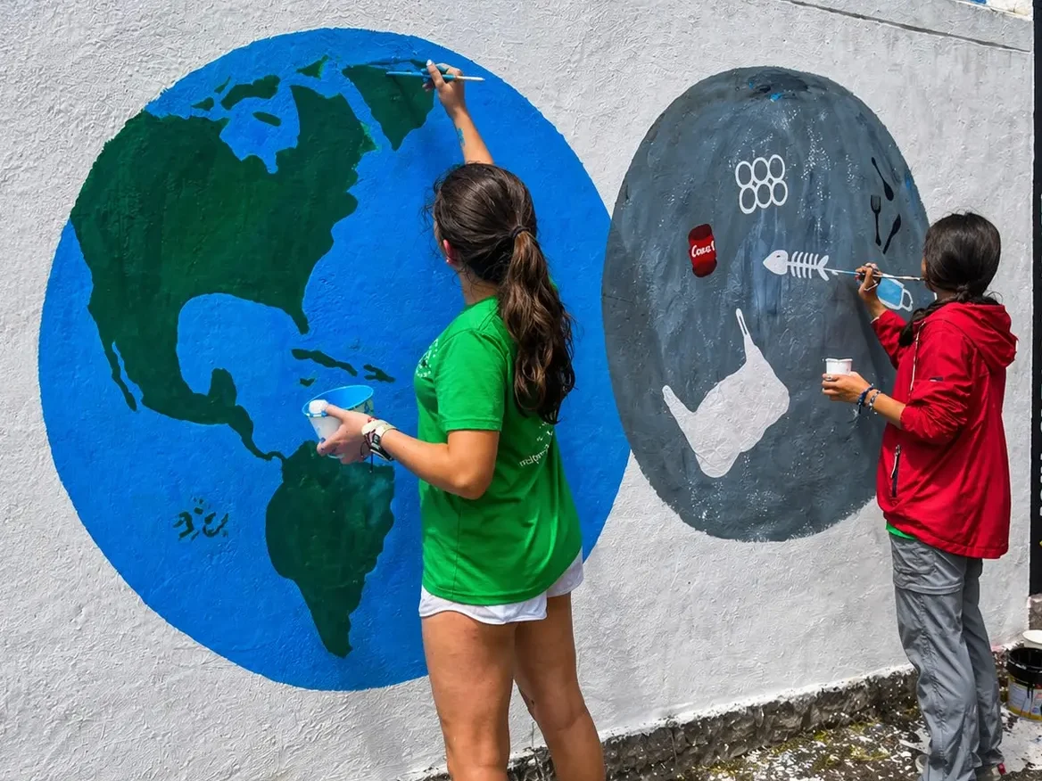 Two young volunteers paint an environmental mural in San Cristóbal, Galápagos, promoting sustainability and conservation awareness.